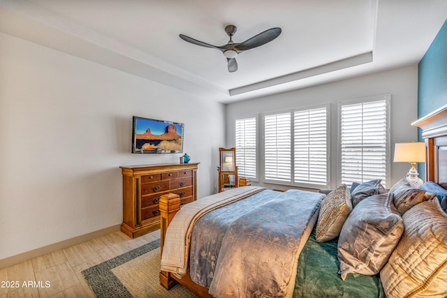 bedroom featuring a raised ceiling, ceiling fan, and light wood-type flooring