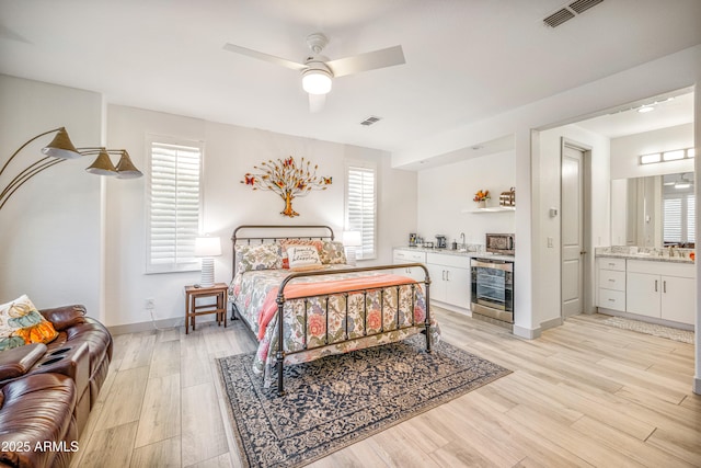 bedroom featuring multiple windows, light wood-type flooring, ceiling fan, and ensuite bath