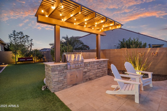 patio terrace at dusk featuring exterior kitchen, a grill, and a yard