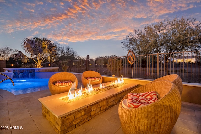 patio terrace at dusk featuring a fenced in pool, pool water feature, and an outdoor fire pit