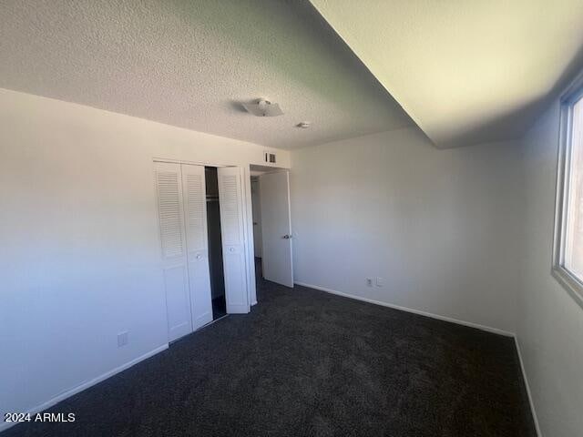 unfurnished bedroom featuring dark carpet, a closet, and a textured ceiling