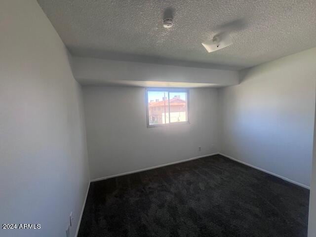 empty room featuring a textured ceiling and dark carpet