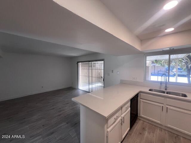 kitchen with white cabinetry, sink, black dishwasher, kitchen peninsula, and dark wood-type flooring