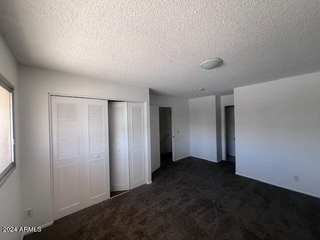 unfurnished bedroom with a textured ceiling, dark colored carpet, and a closet