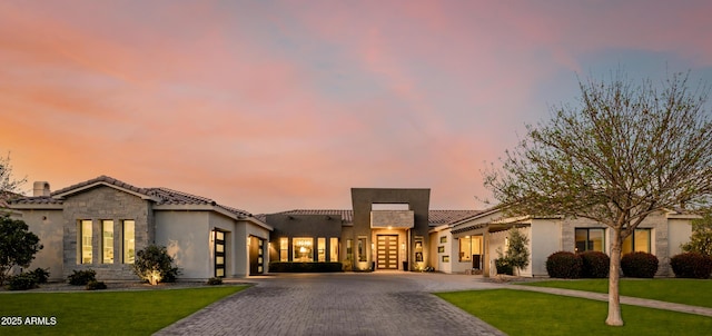 mediterranean / spanish house featuring stone siding, a lawn, decorative driveway, and a tiled roof