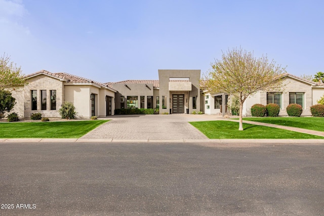 view of front of house featuring decorative driveway, stucco siding, a garage, a tiled roof, and a front lawn