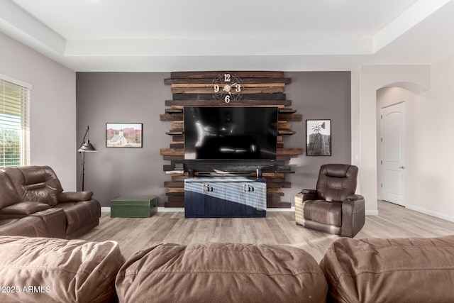 living area featuring a tray ceiling, wood finished floors, and baseboards