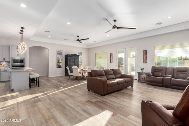 living room featuring light wood-style floors, arched walkways, visible vents, and ceiling fan