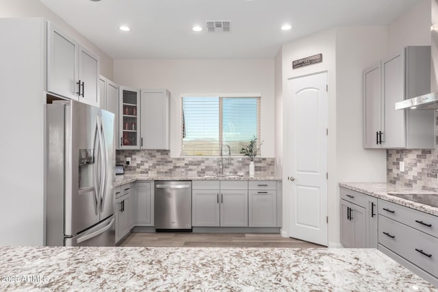 kitchen featuring visible vents, appliances with stainless steel finishes, glass insert cabinets, a sink, and light stone countertops