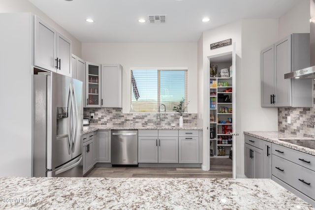 kitchen featuring gray cabinetry, stainless steel appliances, a sink, visible vents, and light stone countertops