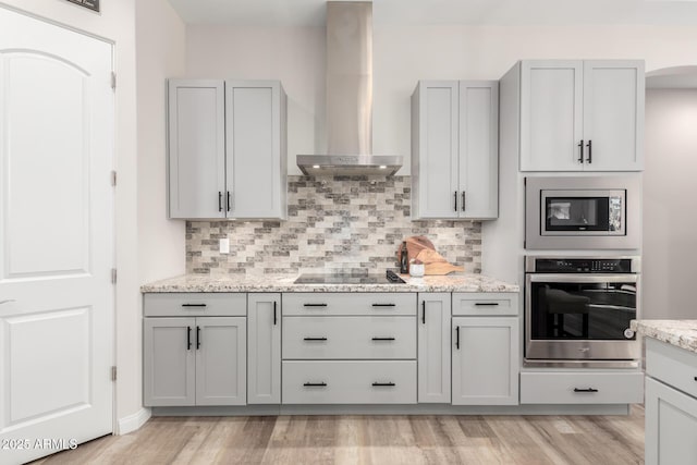 kitchen with stainless steel appliances, tasteful backsplash, light stone countertops, light wood-type flooring, and wall chimney exhaust hood