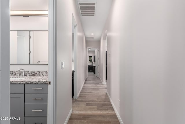 hall featuring light wood-type flooring, baseboards, visible vents, and a sink