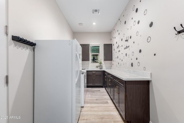 kitchen with dark brown cabinetry, visible vents, light countertops, light wood-type flooring, and freestanding refrigerator