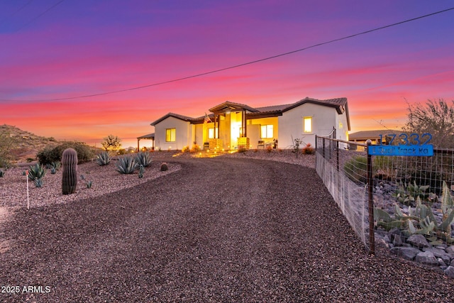 view of front of property with gravel driveway, fence, a tiled roof, and stucco siding