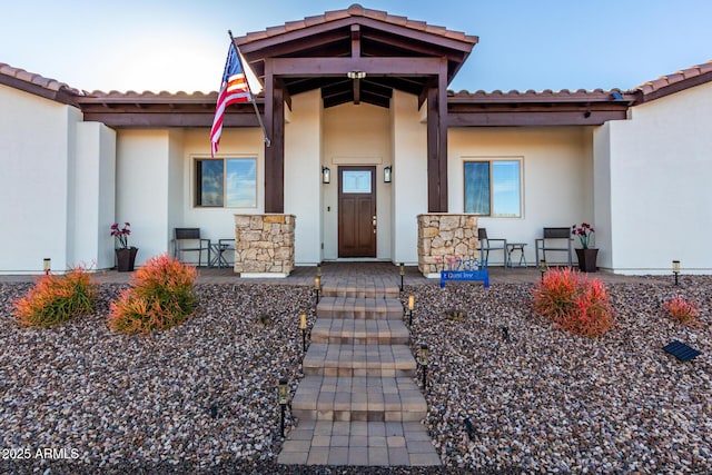 doorway to property featuring a tiled roof, a porch, and stucco siding