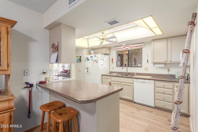 kitchen with white appliances, visible vents, a peninsula, light wood-style floors, and a sink