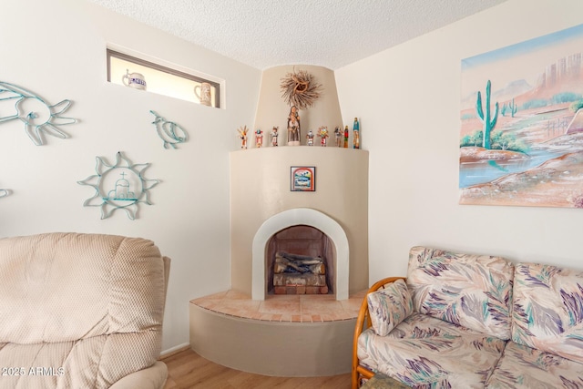 sitting room with a fireplace with raised hearth, a textured ceiling, and wood finished floors