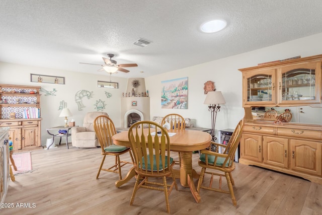 dining area featuring a ceiling fan, light wood-style flooring, visible vents, and a textured ceiling