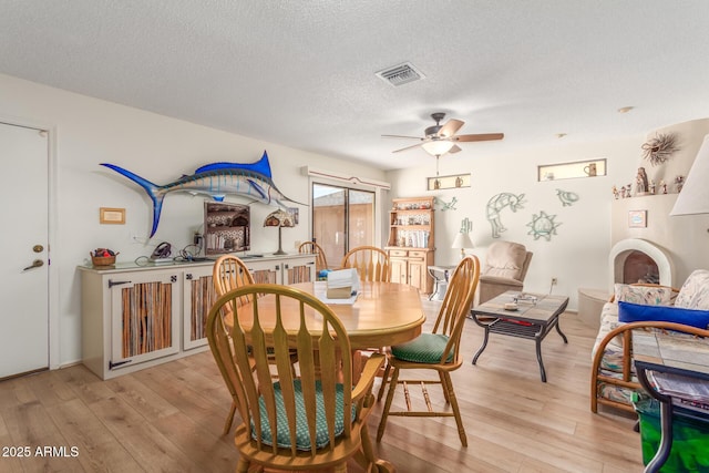 dining room featuring light wood-style floors, a ceiling fan, visible vents, and a textured ceiling