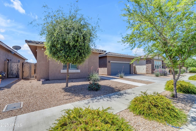view of front of house with a gate, concrete driveway, an attached garage, a tile roof, and stucco siding