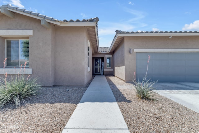 view of exterior entry with a garage, a tile roof, concrete driveway, and stucco siding
