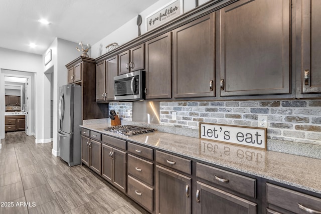 kitchen with stainless steel appliances, tasteful backsplash, baseboards, dark brown cabinetry, and light stone countertops