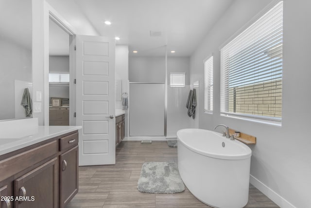 bathroom with recessed lighting, vanity, a walk in shower, baseboards, and a soaking tub