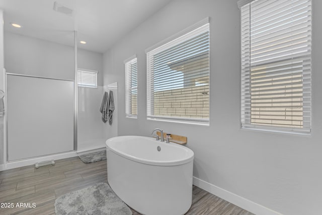 bathroom with a shower stall, wood finished floors, a freestanding tub, baseboards, and recessed lighting