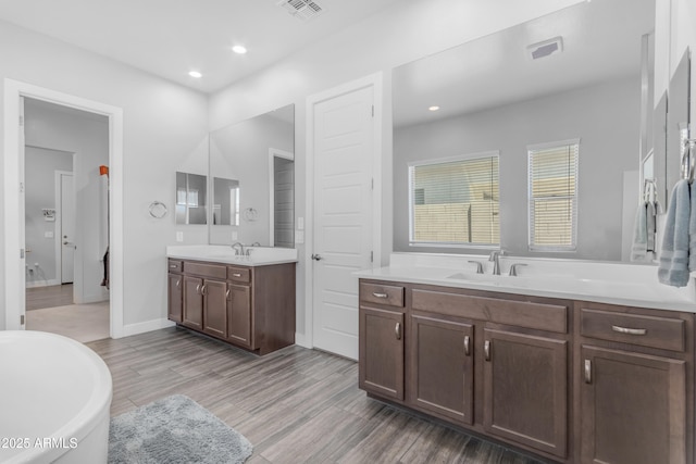 bathroom with two vanities, a soaking tub, visible vents, and a sink