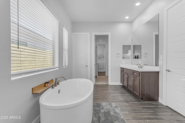 bathroom with recessed lighting, a freestanding bath, wood finished floors, vanity, and baseboards