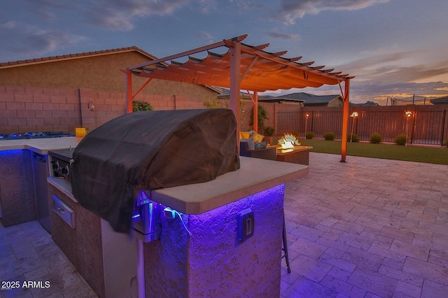 patio terrace at dusk with a fire pit, a pergola, an outdoor kitchen, and a fenced backyard
