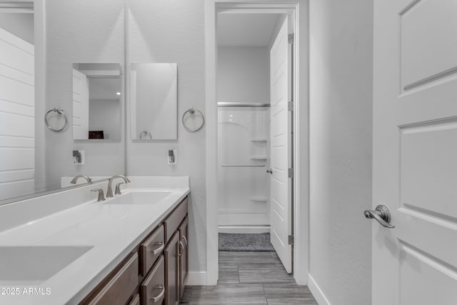 bathroom featuring walk in shower, baseboards, a sink, and double vanity