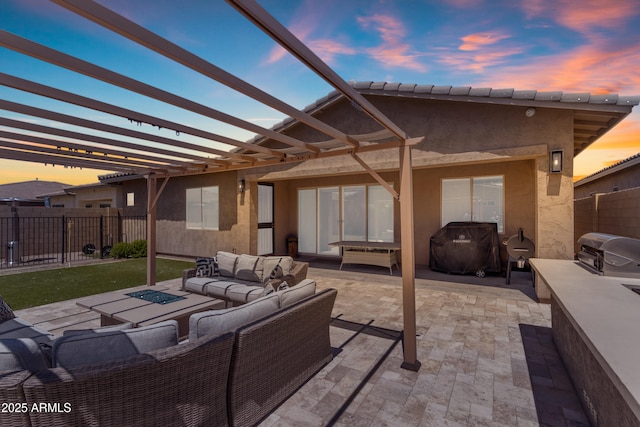 patio terrace at dusk with a pergola, an outdoor living space, fence, a grill, and an outdoor kitchen