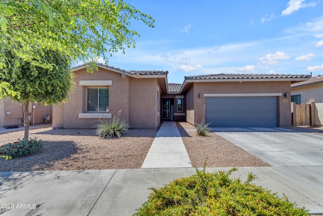 view of front of house with a tile roof, concrete driveway, fence, an attached garage, and stucco siding