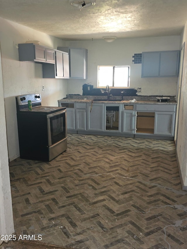 813 N Berry Ave, Winslow, AZ 86047 - kitchen with stainless steel electric range oven, gray cabinets, a textured ceiling, a sink, and brick flooring