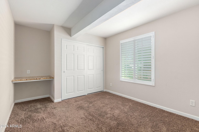 unfurnished bedroom featuring beamed ceiling, carpet, and a closet