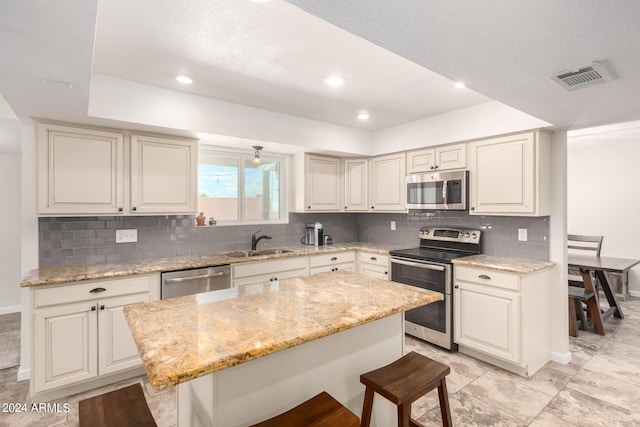 kitchen featuring a kitchen breakfast bar, tasteful backsplash, appliances with stainless steel finishes, sink, and a center island