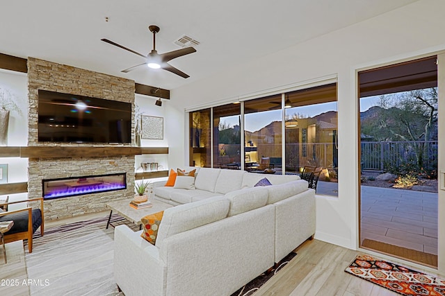 living room featuring visible vents, a wealth of natural light, a ceiling fan, a fireplace, and wood finished floors