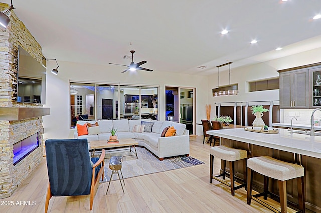 living area featuring light wood finished floors, ceiling fan, a stone fireplace, and recessed lighting