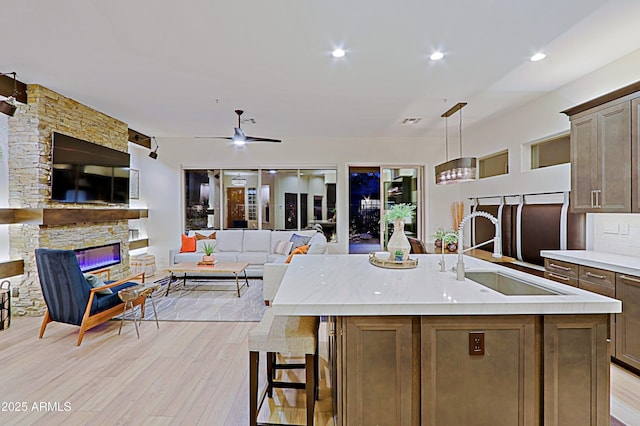 kitchen with a sink, open floor plan, a stone fireplace, light countertops, and light wood-style floors