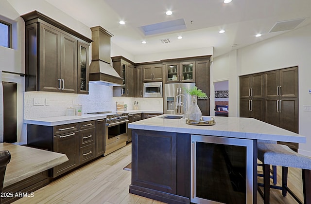 kitchen featuring a kitchen bar, dark brown cabinets, appliances with stainless steel finishes, beverage cooler, and premium range hood