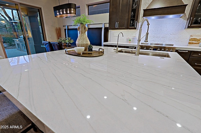 kitchen with glass insert cabinets, dark brown cabinetry, custom exhaust hood, a sink, and decorative backsplash