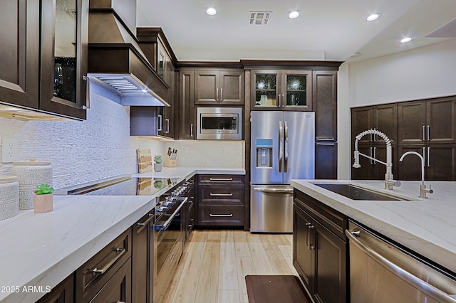 kitchen with light wood-style flooring, dark brown cabinets, appliances with stainless steel finishes, a sink, and custom range hood