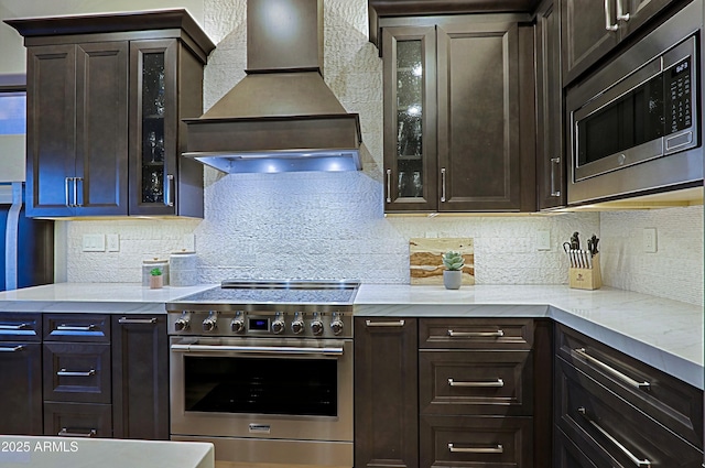 kitchen with stainless steel appliances, dark brown cabinetry, premium range hood, and backsplash