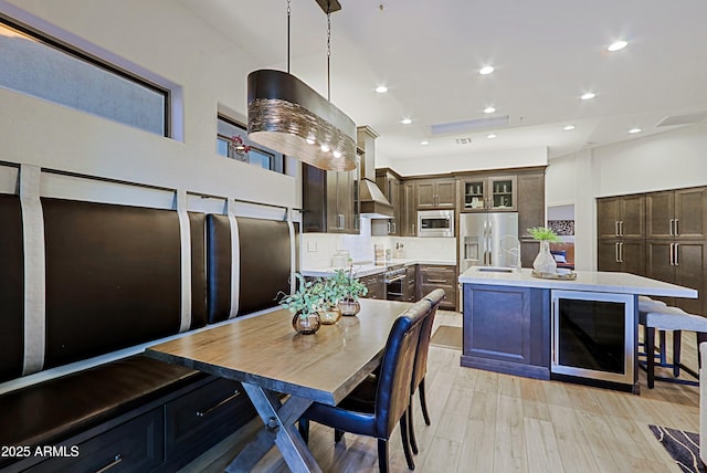 kitchen featuring an island with sink, light wood-style flooring, light countertops, beverage cooler, and stainless steel appliances