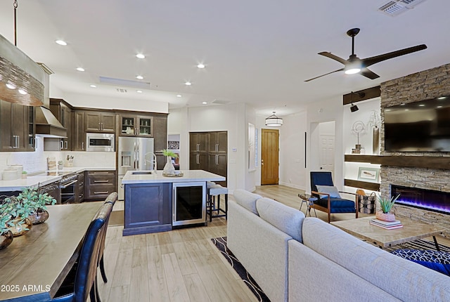 kitchen featuring dark brown cabinetry, light countertops, beverage cooler, stainless steel appliances, and open floor plan