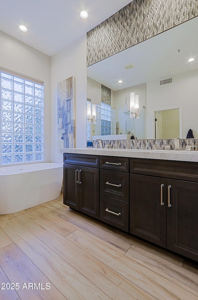 full bath featuring visible vents, recessed lighting, wood finished floors, a freestanding bath, and double vanity