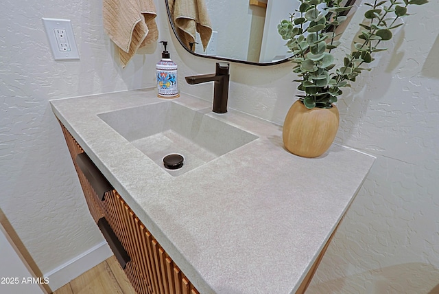 details featuring a textured wall, vanity, baseboards, and wood finished floors