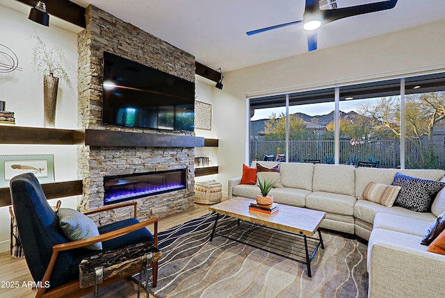 living area with a wealth of natural light, a fireplace, a ceiling fan, and wood finished floors