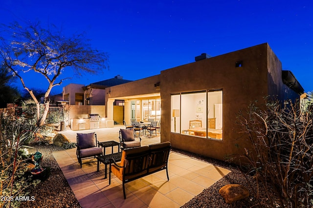 patio at night featuring a grill, fence, and exterior kitchen